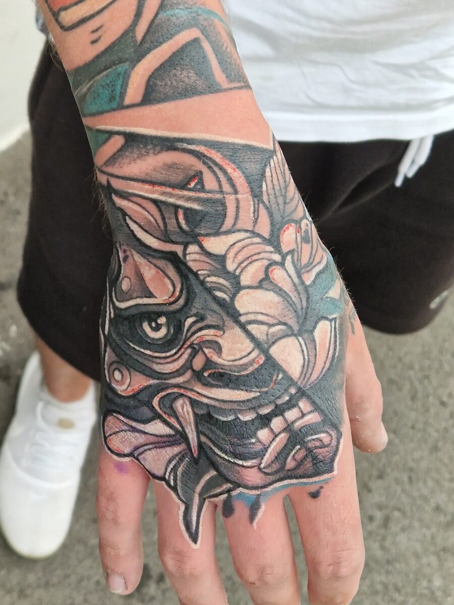 Farbenfrohes Tattoo eines maskierten Gesichts mit Blumen auf der Hand eines Mannes.