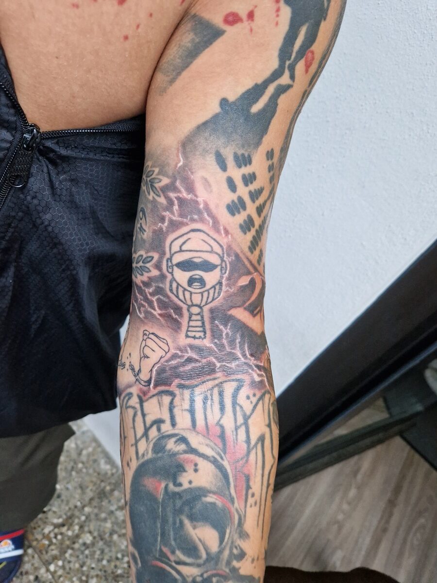 Tätowierter Arm mit Kampfkunstmotiven und einem Comic-Charakter. Bunte und kräftige Farben.