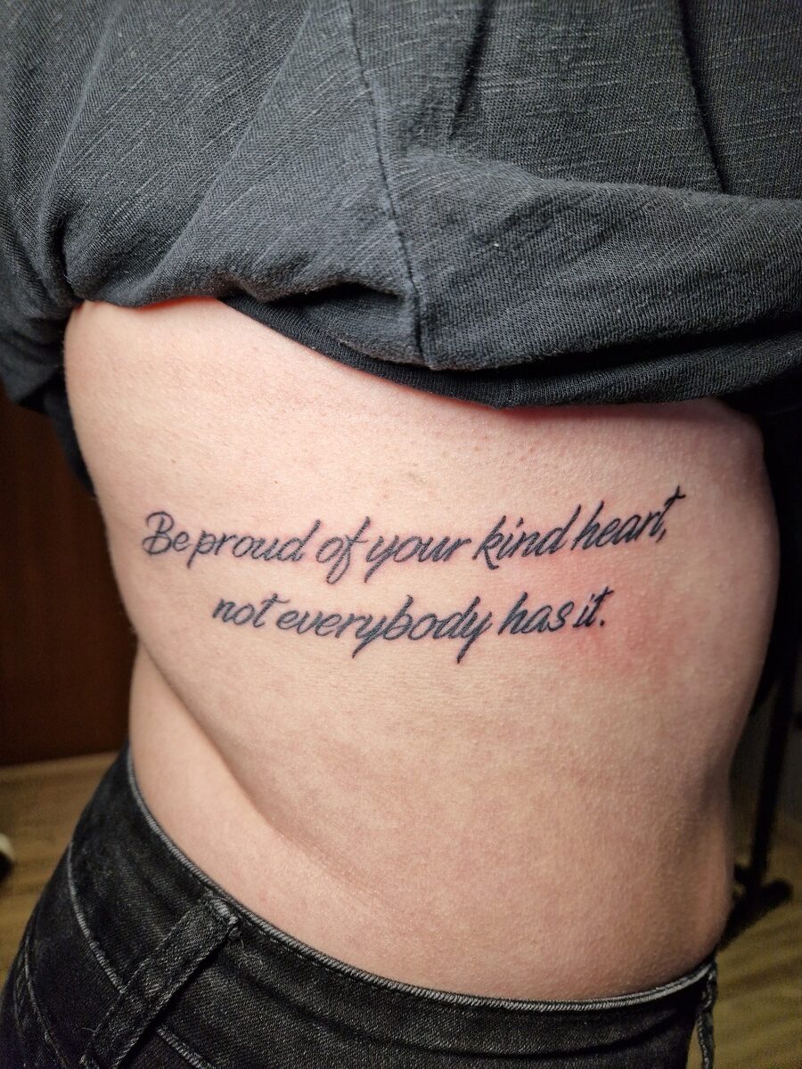 Tätowierung auf der Seite einer Person mit Schriftzug: "Be proud of your kind heart...".
