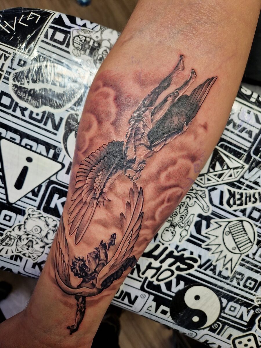 Unterarmtattoo mit zwei geflügelten Figuren auf Wolken, einer kopfüber, beide in schwarz-grau.