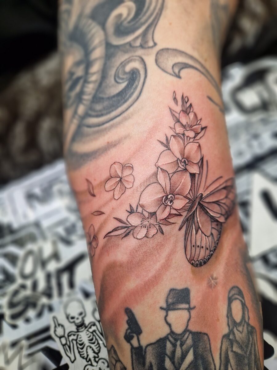 Tätowierter Arm mit Schmetterling, Blumen in Schwarz-Weiß und grafischen Details.