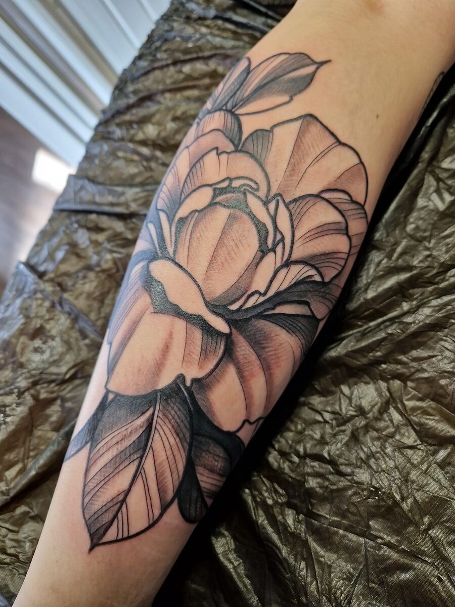 Großes, detailliertes Blumen-Tattoo in Schwarz- und Brauntönen auf einem Unterarm.