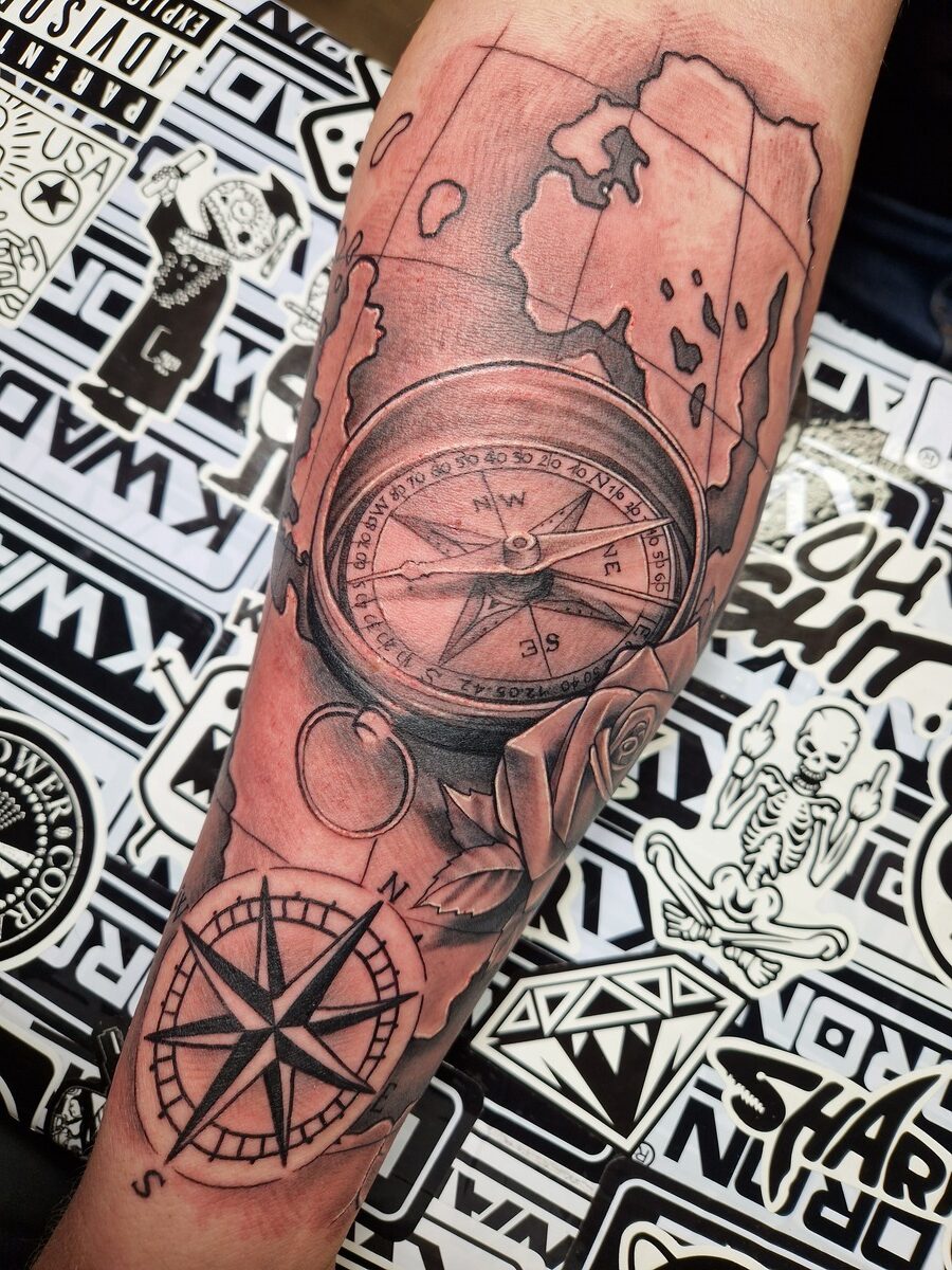 Tattoo auf Arm: Kompass, Karten, Rose; schwarz-weiß, detaillierte Linienkunst.