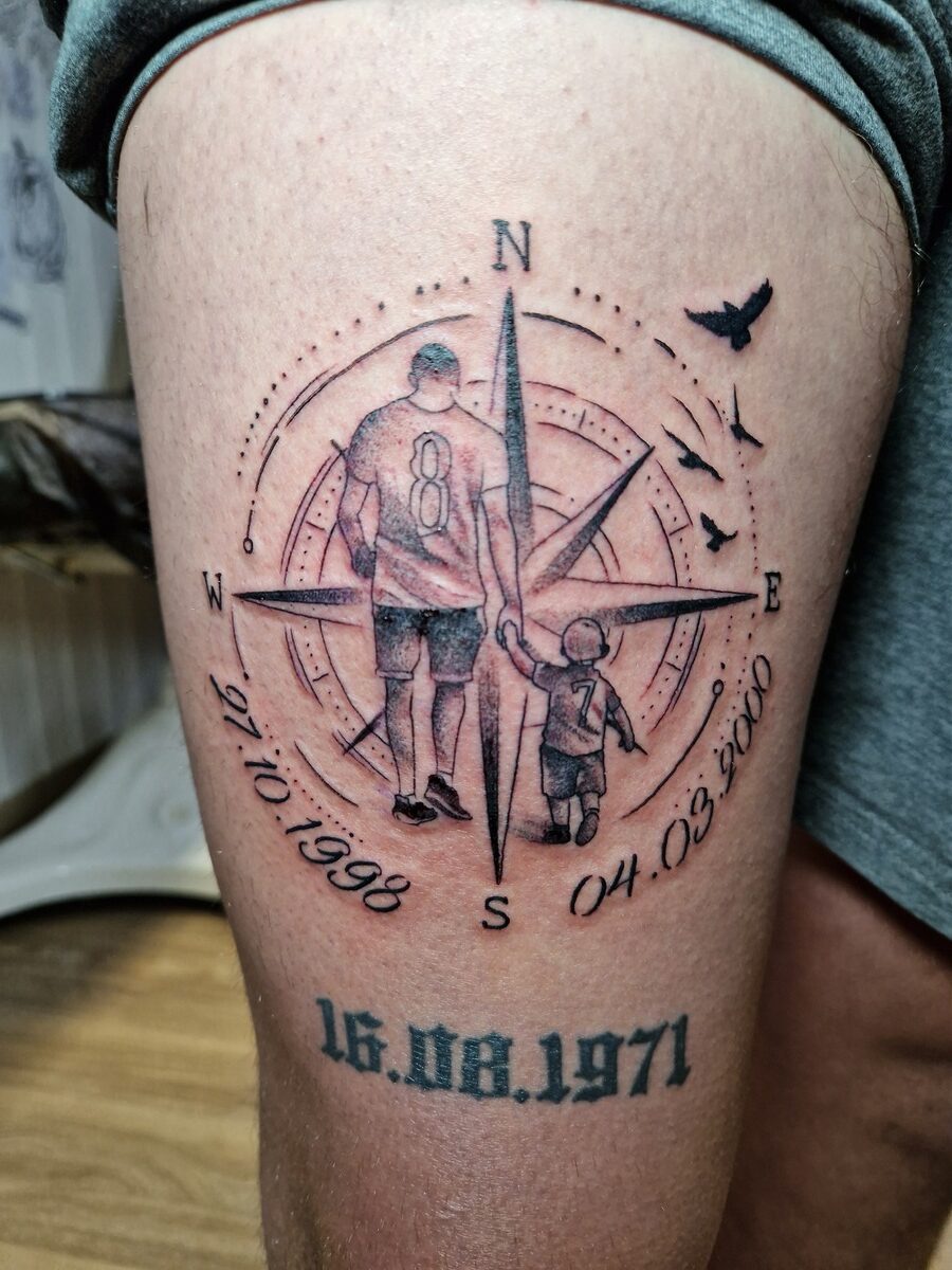 Kompasstattoo mit Vater und Kind, Vögel im Flug, in Schwarz und grauen Tönen auf Bein.