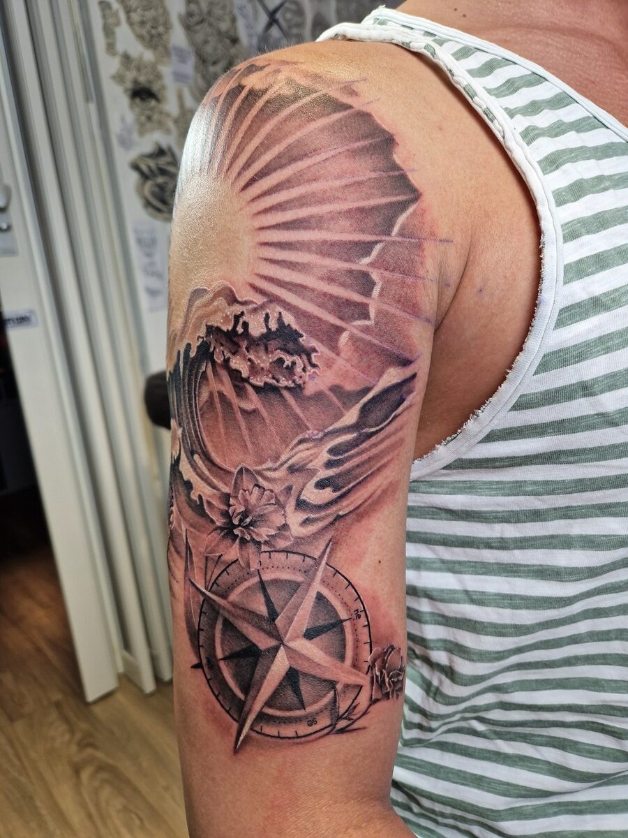 Person mit gestreiftem Shirt zeigt Tattoo: Welle, Kompass und Muscheldesign auf dem Oberarm.