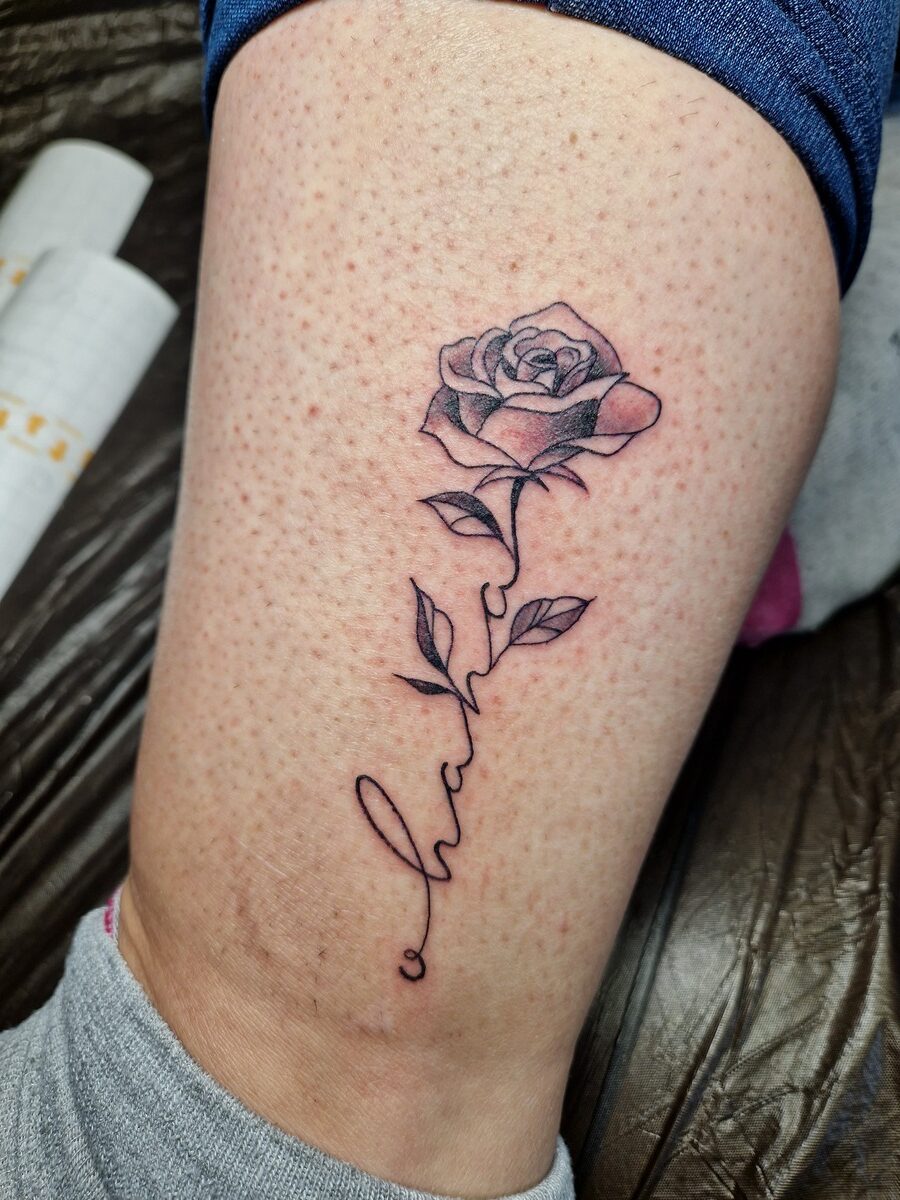 Rose-Tattoo auf Bein, schwarze Tinte, feine Linien, Schriftzug, rosa Haut, Detailaufnahme.