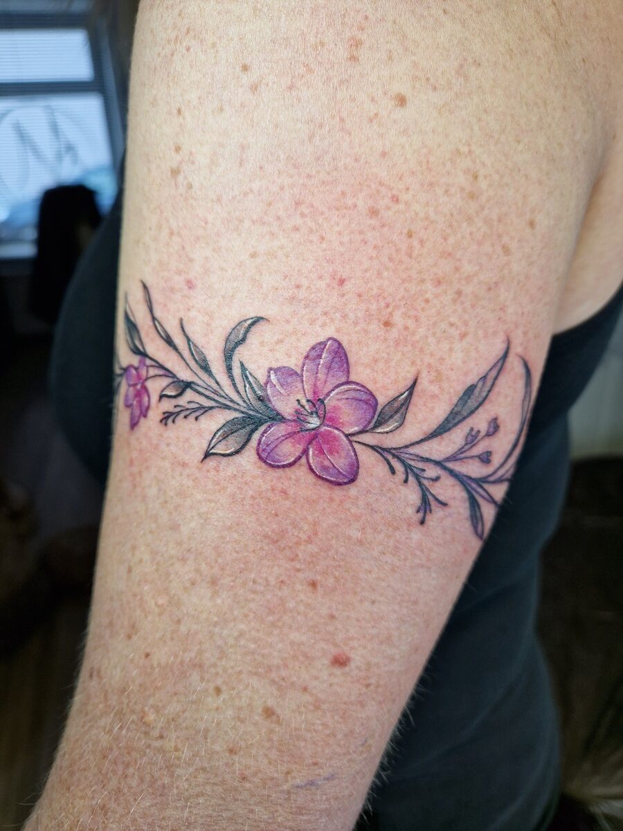 Lila Blumentattoo auf Arm einer Person, schwarz-weiße Blätter, Haut leicht gerötet.