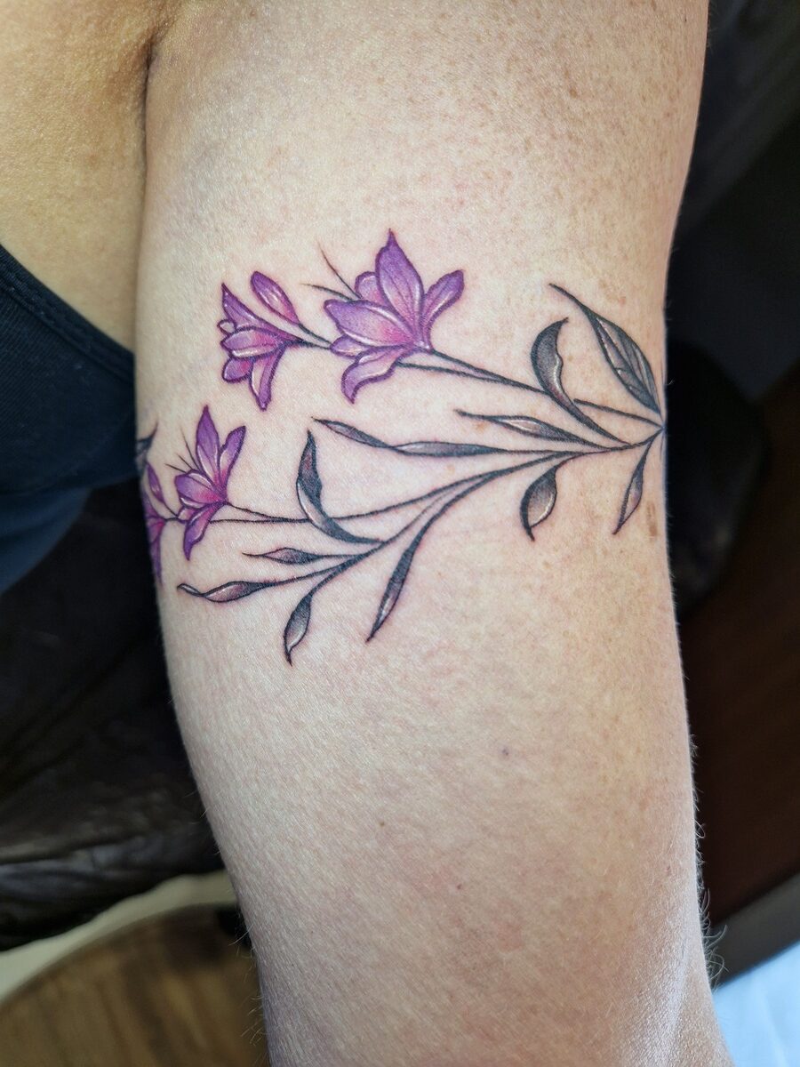 Tätowierung mit lila Blumen auf einem Arm, Haut hell, Blumen haben zarte Linien und Blätter.