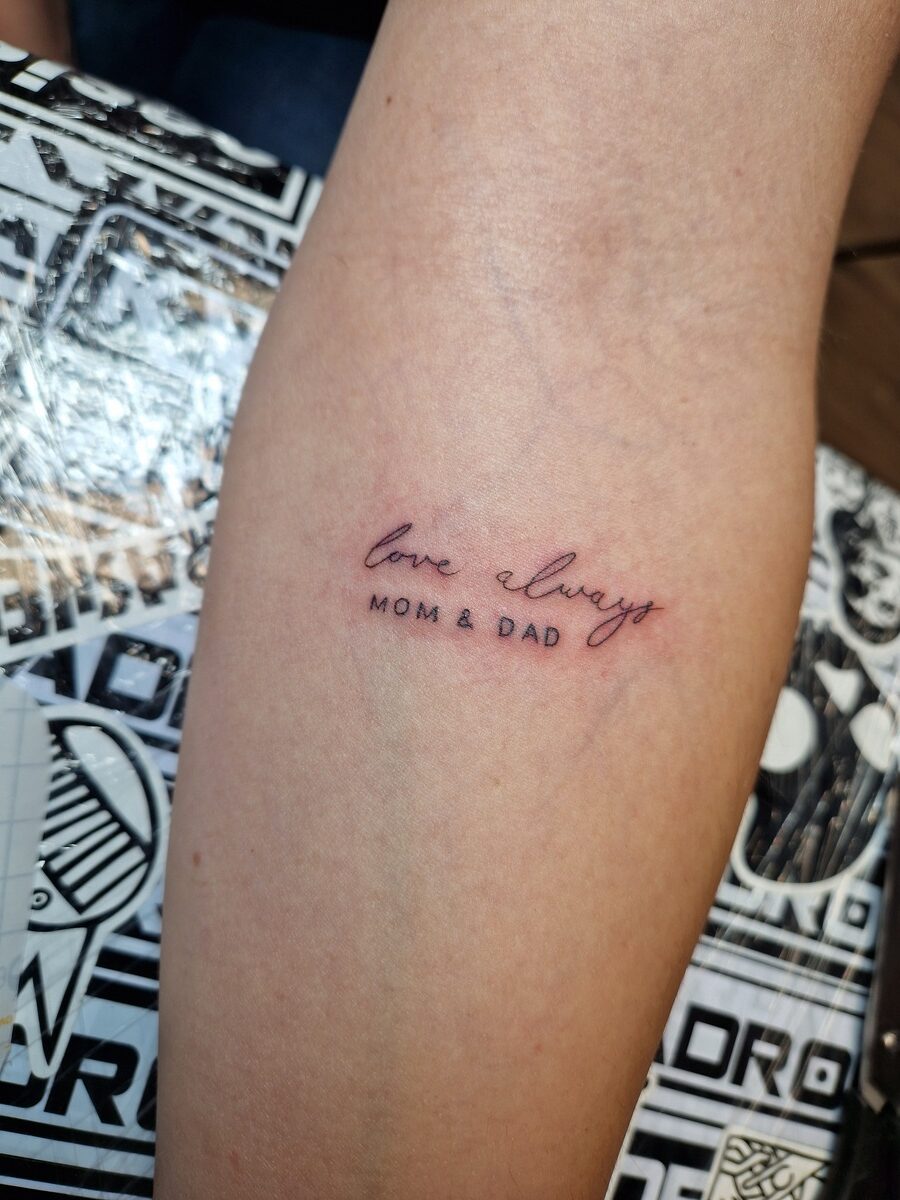 Text-Tattoo auf einem Arm mit den Worten "love always, MOM & DAD".