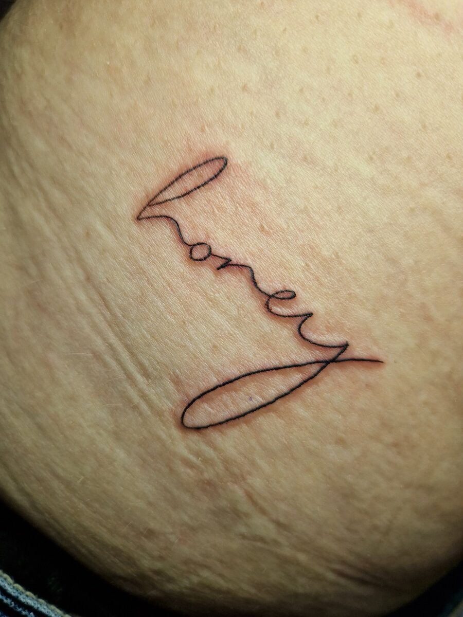 Kleines Tattoo "honey" in geschwungener Schrift auf heller Haut.