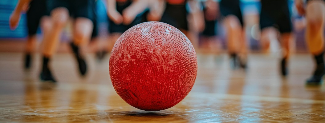 Roter Völkerball auf einem Holzboden mit verschwommenen Spielern im Hintergrund